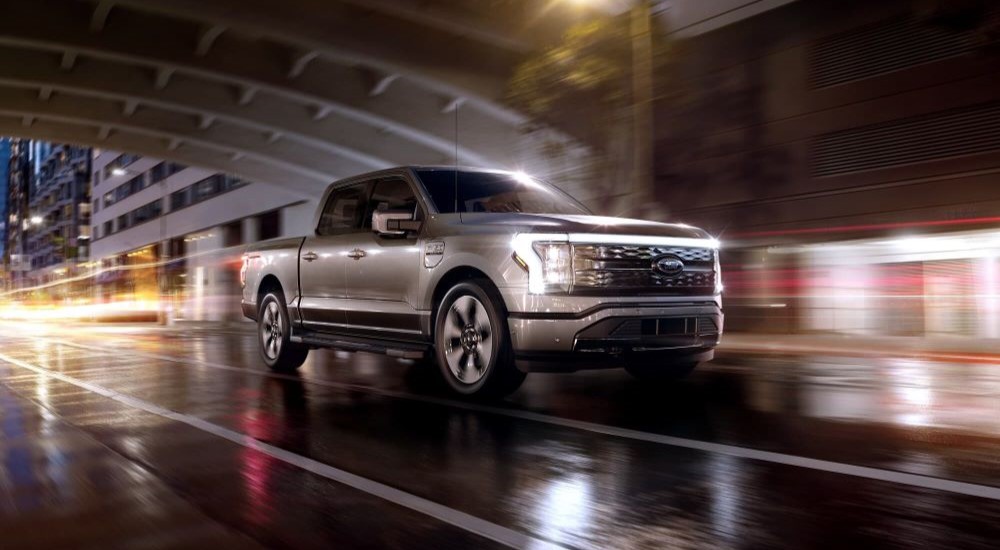 A silver 2023 Ford F-150 Lightning is shown driving on a road.