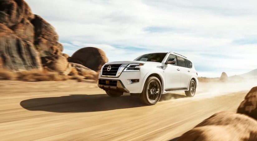 A white 2023 Nissan Armada for sale is shown driving on a sandy trail.