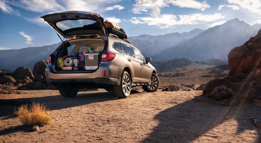 A tan 2015 Subaru Outback is shown with gear in the trunk overlooking rock formations.