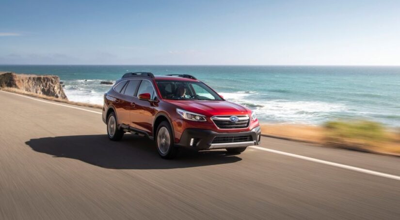 A red 2020 Subaru Outback is driving near the ocean.