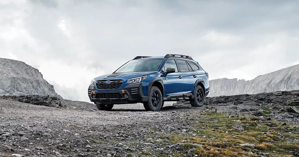 A popular model for Subaru Outback sales, a blue 2022 Subaru Outback Wilderness, is shown parked on a mountain path.