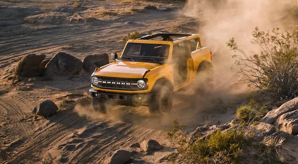 A yellow 2021 Ford Bronco is off-roading on a dusty trail.