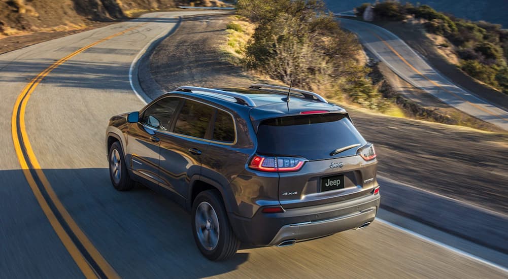 A gray 2020 Jeep Cherokee is shown driving along a winding mountain road.