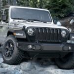 A silver 2020 Jeep Wrangler Willys is shown off-roading on a rocky trail.