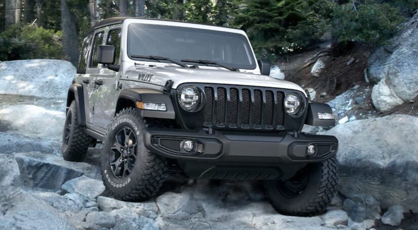 A silver 2020 Jeep Wrangler Willys is shown off-roading on a rocky trail.