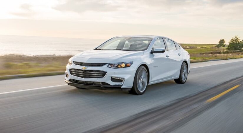 A white 2016 Chevy Malibu is shown driving on a highway to check out used car sales.