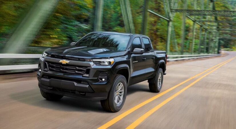 A black 2023 Chevy Colorado is shown driving over a bridge on a forest road.