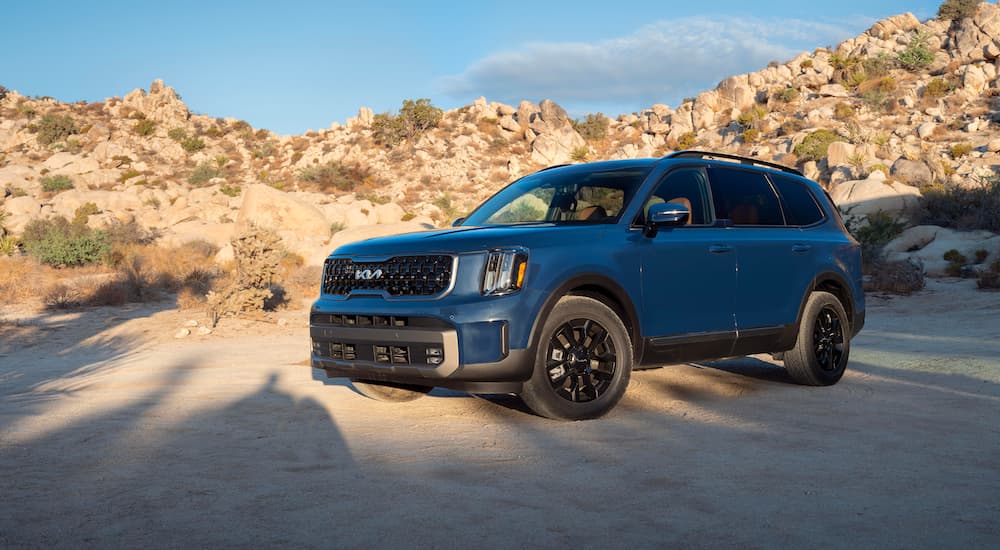A blue 2023 KIA Telluride is shown parked on the sand.