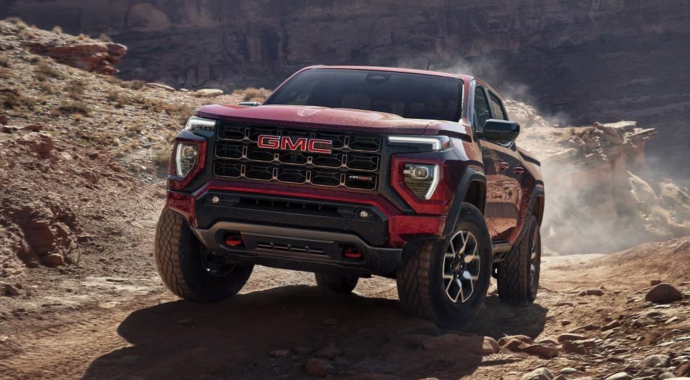 A red 2023 GMC Canyon AT4X is shown driving up a dusty off-road trail. 