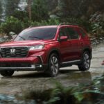 A red 2023 Honda Pilot is shown driving down a trail in the rain.