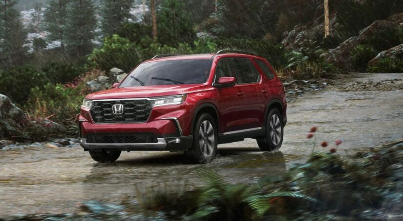 A red 2023 Honda Pilot is shown driving down a trail in the rain.