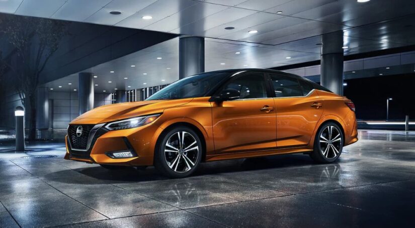 An orange and black 2023 Nissan Sentra is parked in a parking garage at night.