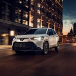 A white 2023 Toyota Corolla Cross is shown driving on a street at night.