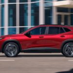 A red 2024 Chevy Trax is shown driving on a road.