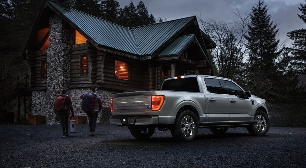 A silver 2023 Ford F-150 Platinum is shown parked near a log cabin after visiting a Ford F-150 dealer.