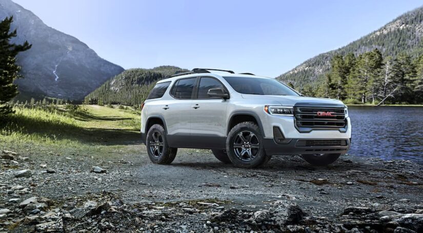 A white 2023 GMC Acadia for sale is shown parked off-road near a river.
