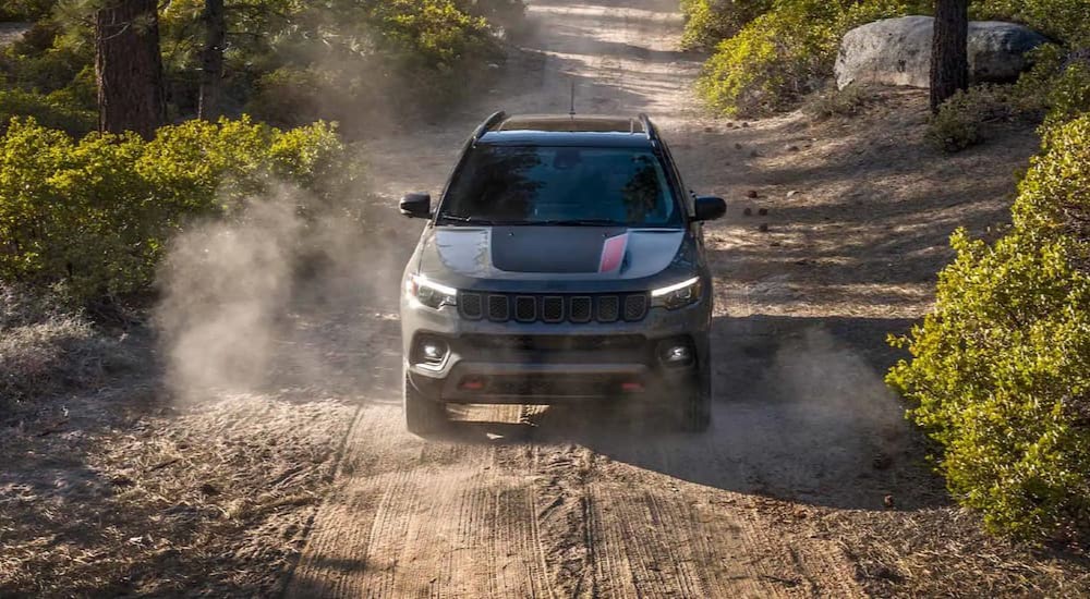 A dark gray 2023 Jeep Compass Trailhawk is shown off-roading on a dirt road.
