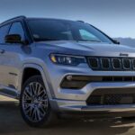 A silver 2023 Jeep Compass for sale is shown parked off road.