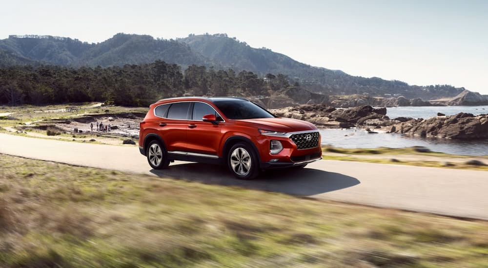 A red 2019 Hyundai Santa Fe is shown driving on a road near water.