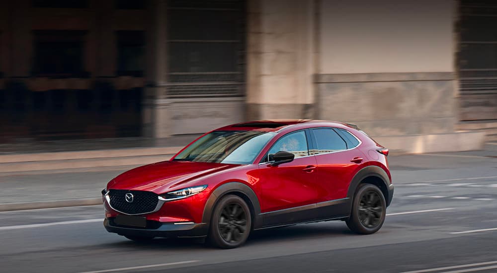A red 2023 Mazda CX-30 is shown driving on a city street.