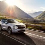 A silver 2023 Mitsubishi Outlander PHEV for sale is shown driving on a road.