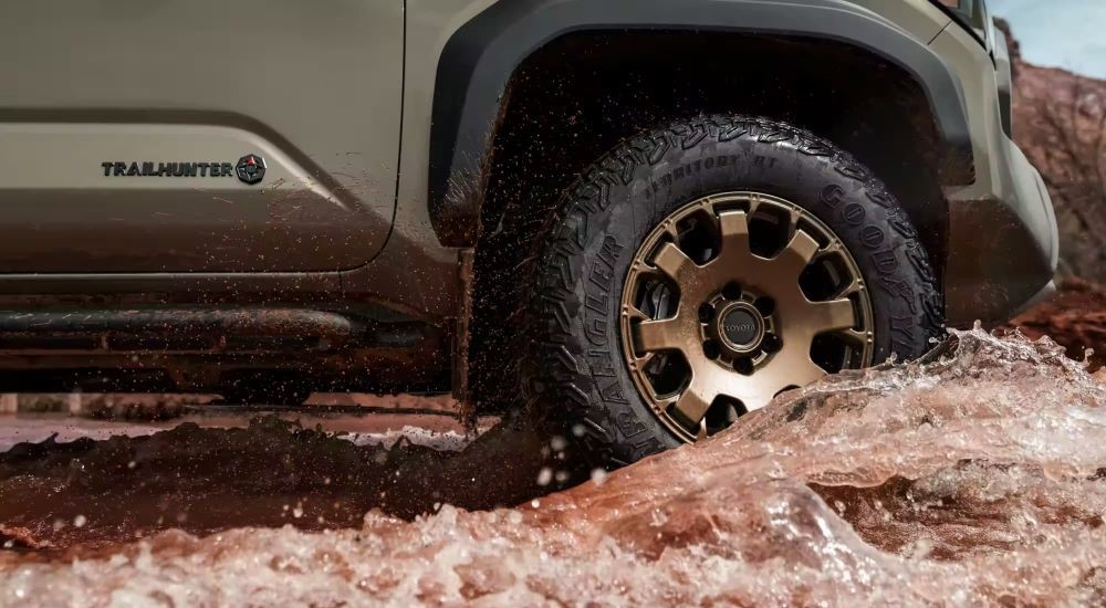A bronze wheel is shown on a 2024 Toyota Tacoma Trailhunter is shown splashing through water.