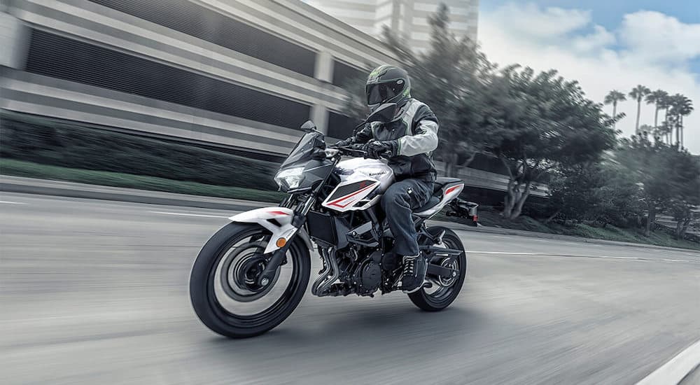 A white, black, and red 2023 Kawasaki Z400 is shown driving on a road.