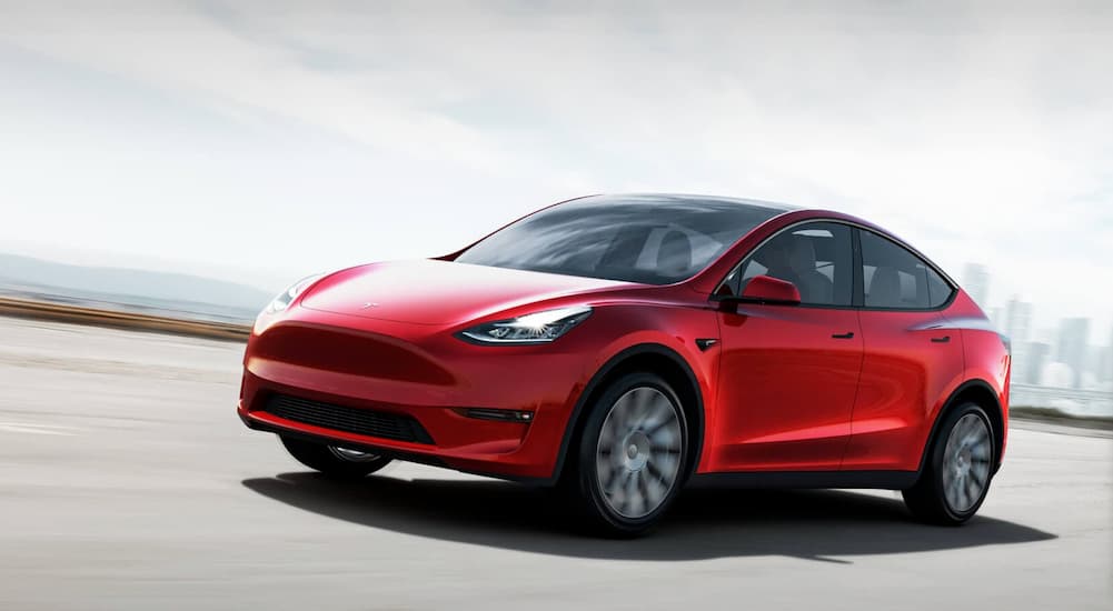 A red 2021 Tesla Model Y is shown driving near a city.
