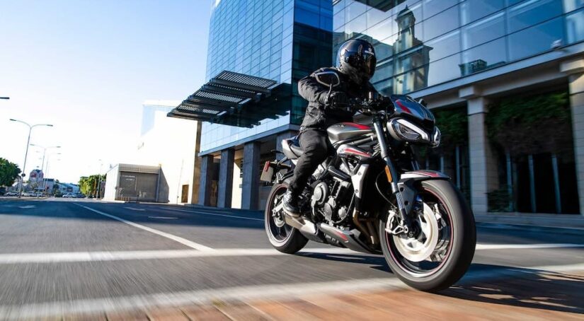 A silver and red 2024 Street Triple R is shown driving near a building.