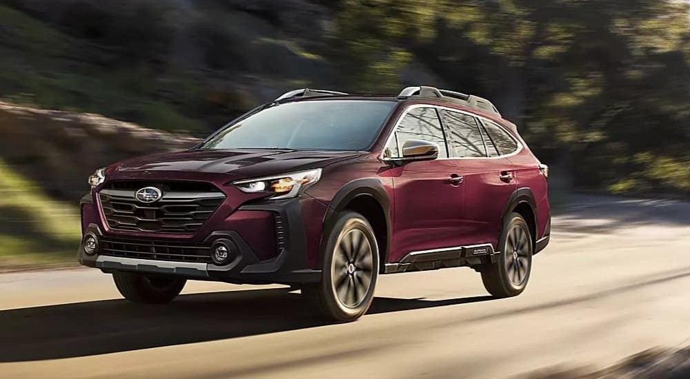 A burgandy 2023 Subaru Outback is shown driving on a road after visiting a used cars dealership.