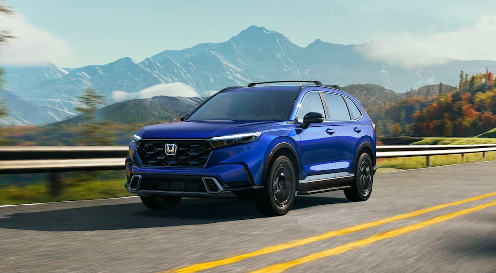 A blue Honda CR-V Hybrid Sport Touring is shown driving on a highway.