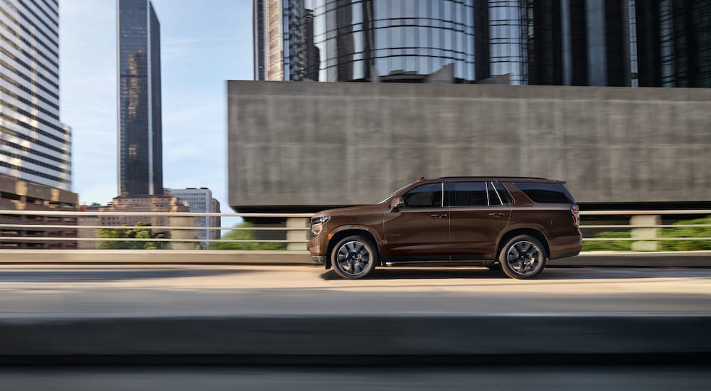 A brown 2023 Chevy Tahoe is shown driving on a bridge.