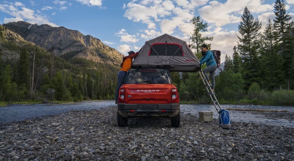 A red 2023 Ford Bronco is shown parked off-road with a roof tent attached.