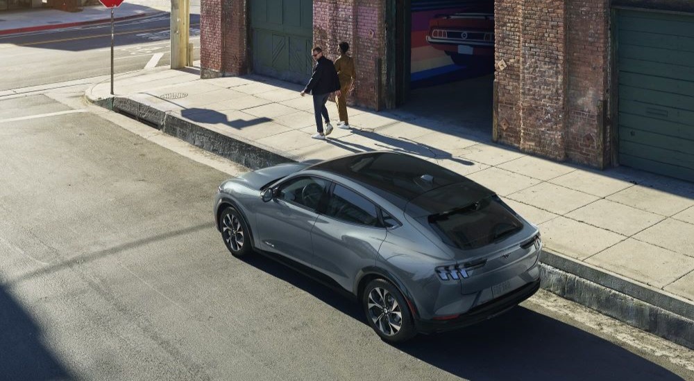 A gray 2023 Ford Mustang Mach-E is shown parked near a corner on a street.