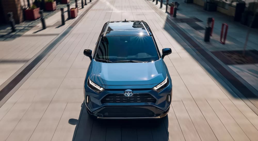 A blue 2023 Toyota RAV4 is shown driving near stores.
