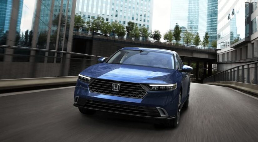 A blue 2023 Honda Accord Sport Hybrid is shown driving on a city street.