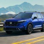 A blue 2023 Honda CR-V Hybrid Sport Touring is shown driving near mountains.