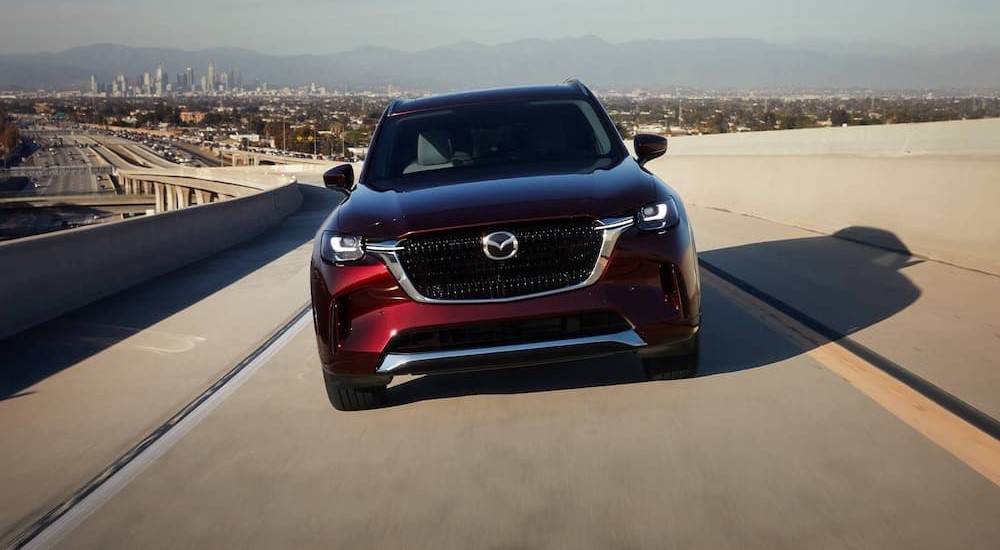 A burgundy 2024 Mazda CX-90 is shown driving on an on ramp.