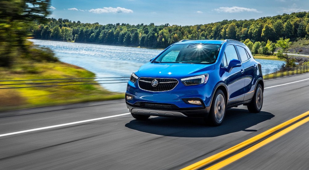 A blue 2018 Buick Encore is shown driving near a lake.