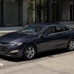 A blue 2023 Chevy Malibu is shown parked on a street after visiting a Chevrolet dealer.