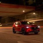 A red 2023 Mazda CX-5 for sale is shown driving on a city street at night.