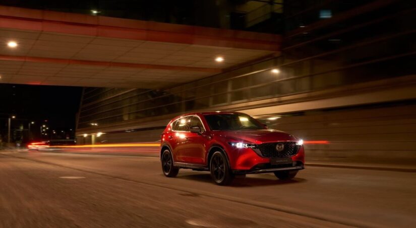 A red 2023 Mazda CX-5 for sale is shown driving on a city street at night.