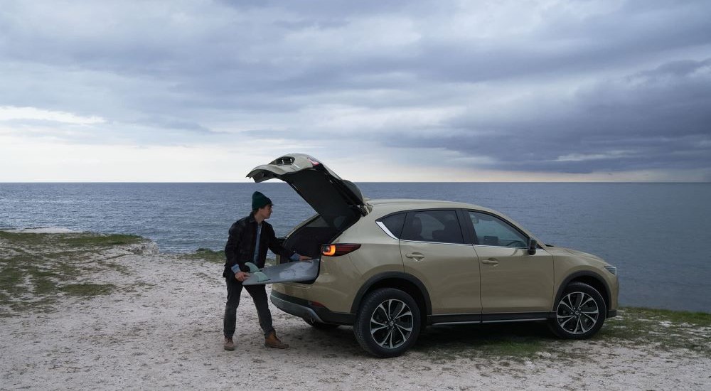 A person is shown removing a surfboard from a green 2023 Mazda CX-5.