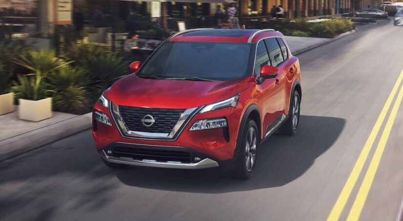 A red 2023 Nissan Rogue for sale is shown driving on a road.