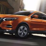 An orange 2023 Nissan Qashqai is shown driving on a street.