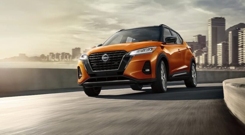 An orange 2023 Nissan Kicks is shown driving on a road after visiting a Nissan dealer.