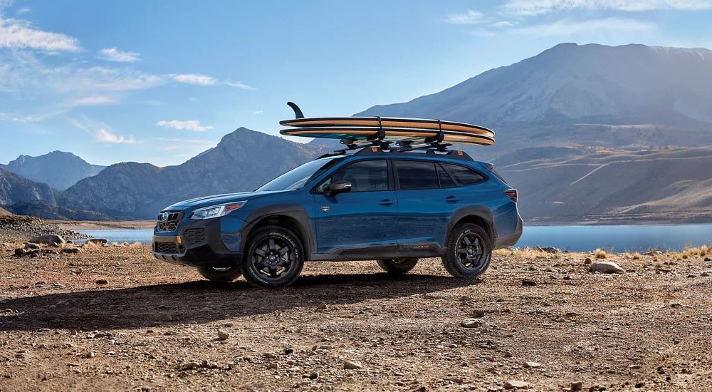 A blue 2024 Subaru Outback Wilderness is shown near a lake and mountains.