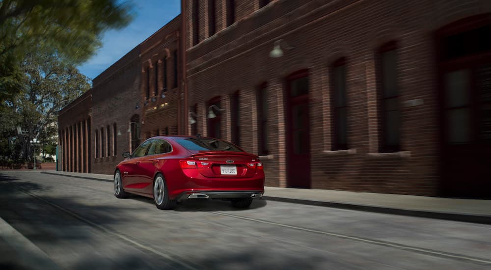 A red 2023 Chevy Malibu RS is shown from the rear at an angle on a city street.