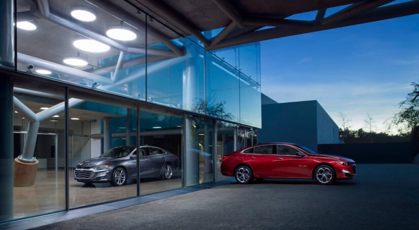 A silver and a red 2023 Chevy Malibu are shown at a dealership.