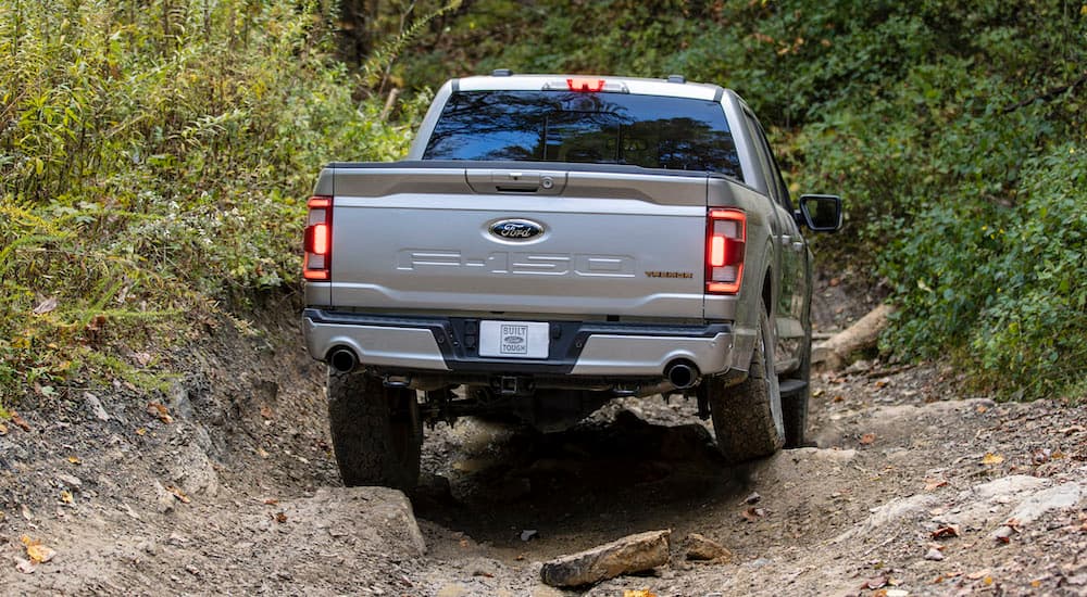 A silver 2021 Ford F-150 Tremor is shown from the rear while driving over a rocky surface.